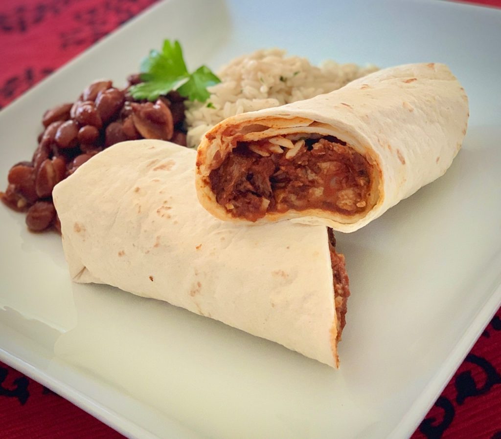 Chile Colorado burrito cut in half on a white plate