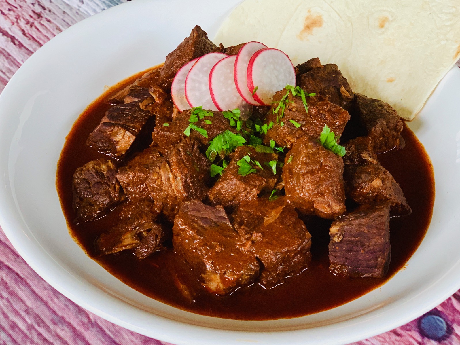 Chili Colorado in white bowl with radish slices