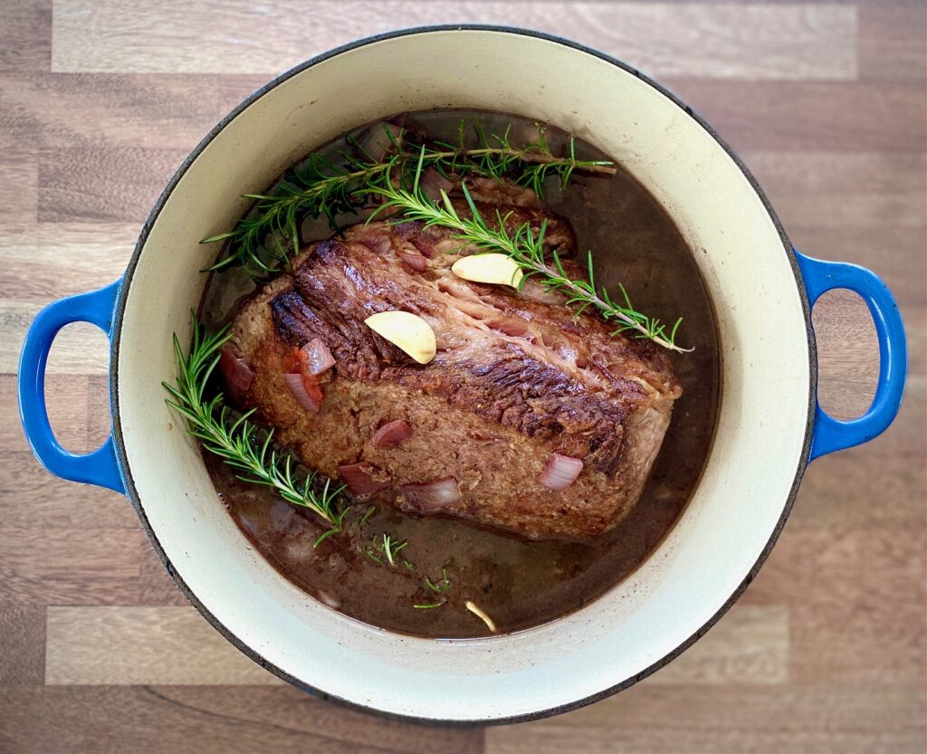 seared meat, garlic and rosemary in pot with liquid